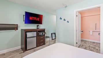 A bedroom with a bed, a TV mounted on the wall, a dresser, and a door leading to a bathroom.