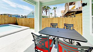 A covered patio with a pool, outdoor furniture, and a view of a wooden fence and buildings in the background. - PRIVATE Heated POOL!!!  Endless Summer is just blocks from the beach!! (Port Aransas)