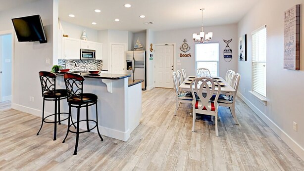 A spacious kitchen with a central island, a dining area with a large table and chairs, and a living area with a TV mounted on the wall. - PRIVATE Heated POOL!!!  Endless Summer is just blocks from the beach!! (Port Aransas)