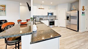 A modern kitchen with a granite countertop, stainless steel appliances, and a dining area with wooden chairs. - PRIVATE Heated POOL!!!  Endless Summer is just blocks from the beach!! (Port Aransas)