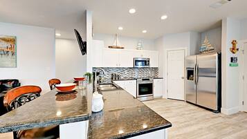 A modern kitchen with a granite countertop, stainless steel appliances, and a dining area with wooden chairs.