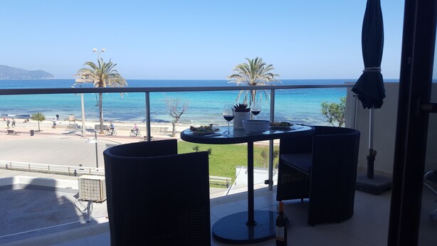 Ein Balkon mit Esstisch, mit Blick auf einen Strand mit Palmen und das Meer.