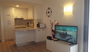 Eine moderne Küche mit weißen Schränken, einer Mikrowelle und einem Spülbecken. An der Wand hängt eine Uhr und ein Flachbildfernseher ist angebracht.