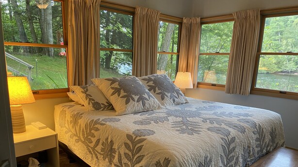 A bedroom with a large bed, two bedside lamps, a nightstand, and a window with curtains. - Muskegon River Front Cabin  (Newaygo)
