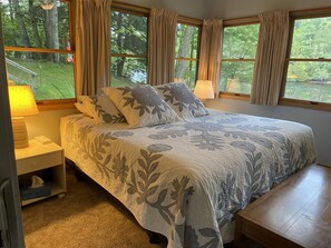 A bedroom with a large bed, two bedside lamps, a nightstand, and a window with curtains. - Muskegon River Front Cabin (Newaygo)