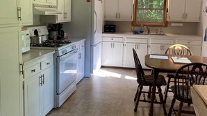 A kitchen with white cabinets, a stove, and a dining area with a table and chairs. - Muskegon River Front Cabin  (Newaygo)