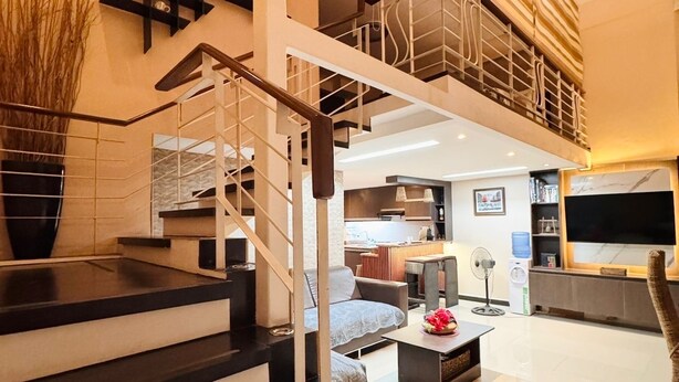 Un interior moderno con una escalera que conduce a un nivel superior, una sala de estar con sofá, mesa de centro y televisor.