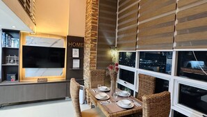 Un comedor moderno con una mesa alta dispuesta para cuatro personas, rodeado de sillas de mimbre. Un ventanal ofrece vistas de la ciudad de noche.