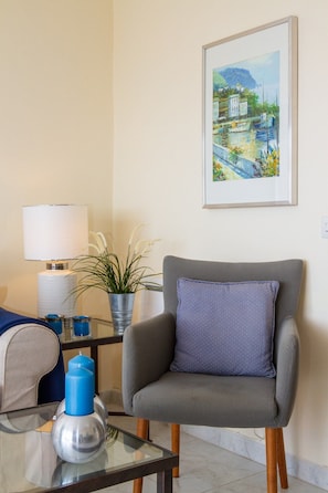 A room with a grey armchair, a small table with a lamp, a framed painting, and a potted plant. - Riviera Playa | Charming Apartment with Sea Views, Terrace & Pools (Mijas Costa)