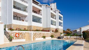 A swimming pool adjacent to a multi-story building with balconies, stone accents, and a lifebuoy. - Riviera Playa - Costa del Sol - Charming apartment with Sea View (Mijas Costa)