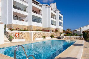 Une piscine située à côté d’un immeuble à plusieurs étages, doté de balcons, d’une façade en pierre et d’une bouée de sauvetage fixée au mur.