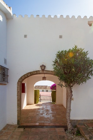An arched entrance with a tiled pathway leading to a building with a tiled roof. - Riviera Playa | Charming Apartment with Sea Views, Terrace & Pools (Mijas Costa)
