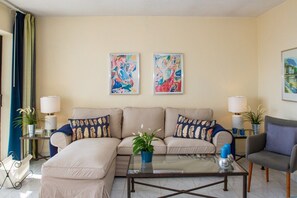 A living room with a sofa set, two side tables with lamps, a coffee table, and two abstract paintings on the wall. - Riviera Playa | Charming Apartment with Sea Views, Terrace & Pools (Mijas Costa)