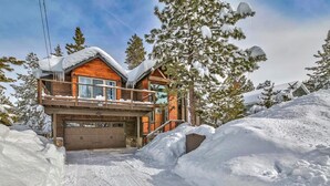Un'accogliente baita in legno a due piani con un garage, immersa tra alberi innevati e un vialetto coperto di neve.