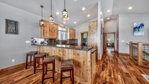 Una cucina moderna con mobili in legno, un'isola centrale con sgabelli, illuminazione a sospensione e vista sull'area living.