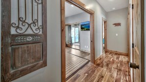 Un corridoio con pavimento in legno, una porta metallica decorativa e vista su una stanza con una grande finestra e un quadro.