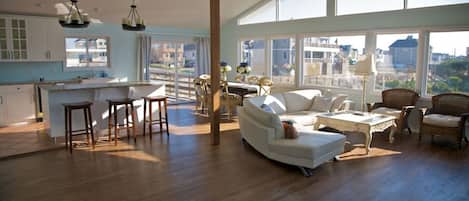 A spacious living area with a large window, a kitchen with white cabinets, and a dining area with wicker furniture.