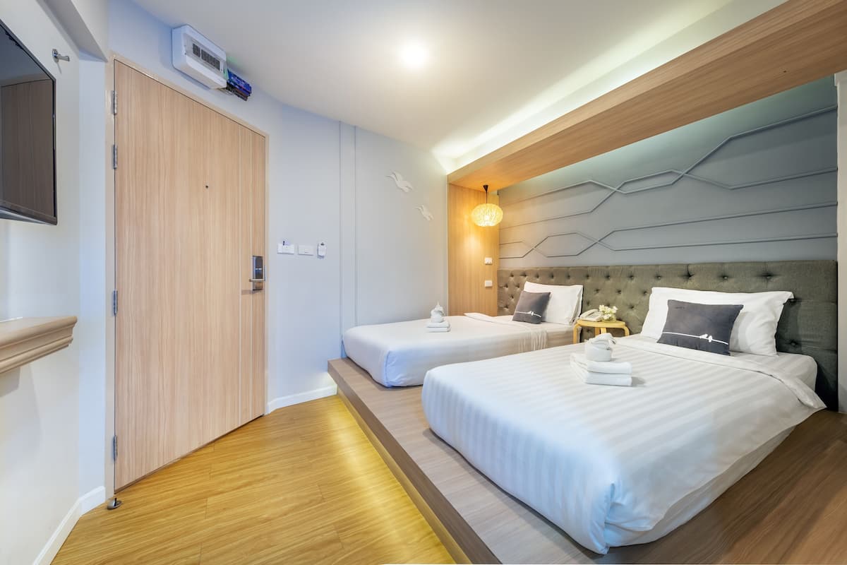 Une chambre d’hôtel avec deux lits, une télévision, une armoire et une table de chevet avec une lampe.