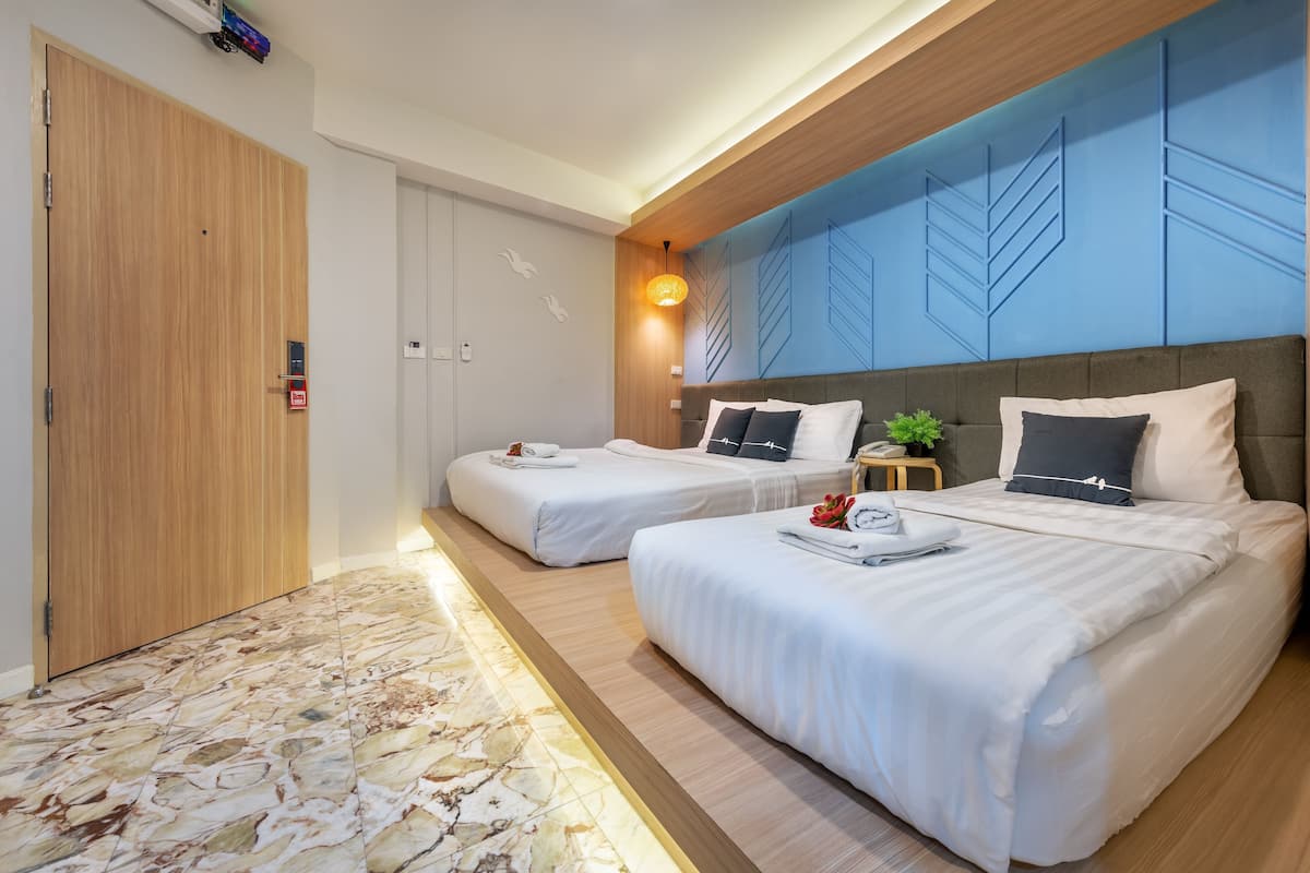 Une chambre d’hôtel avec deux lits, une porte en bois, un sol en marbre et un mur d’accent bleu.