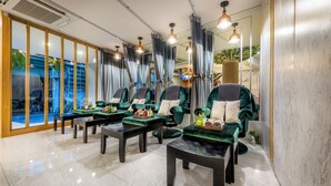 A spa room with multiple green chairs, black tables, and a large window with curtains. - Tori Prestige Bangkok Hotel (Bangkok)