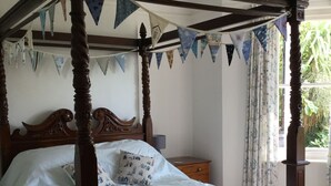 Una cama con dosel, una mesita de noche y una ventana con cortinas.