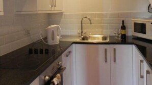 Cocina compacta con armarios blancos, encimera negra, microondas, fregadero y hervidor.