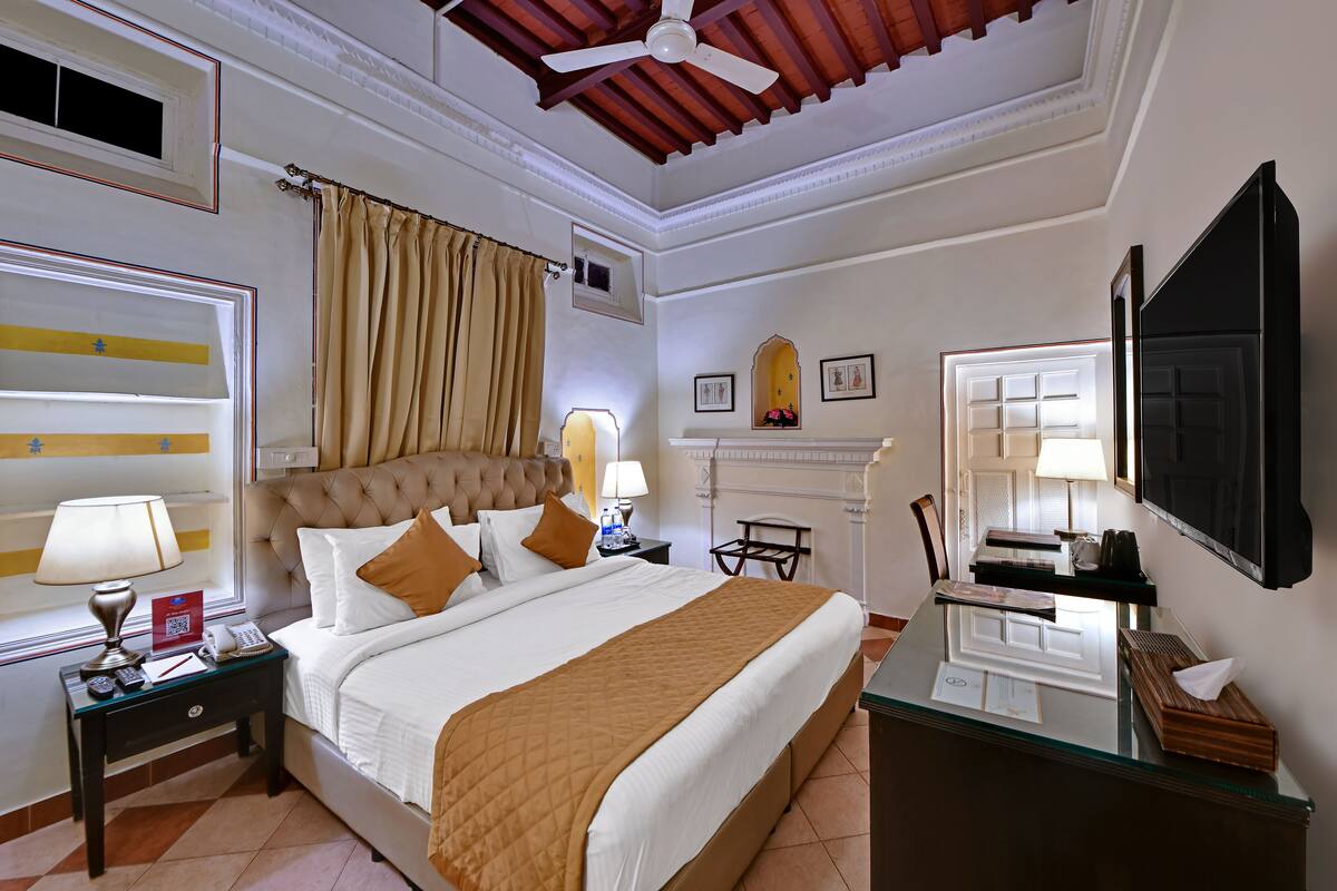 A hotel room with a bed, bedside tables, a desk, a television, and a fireplace.
