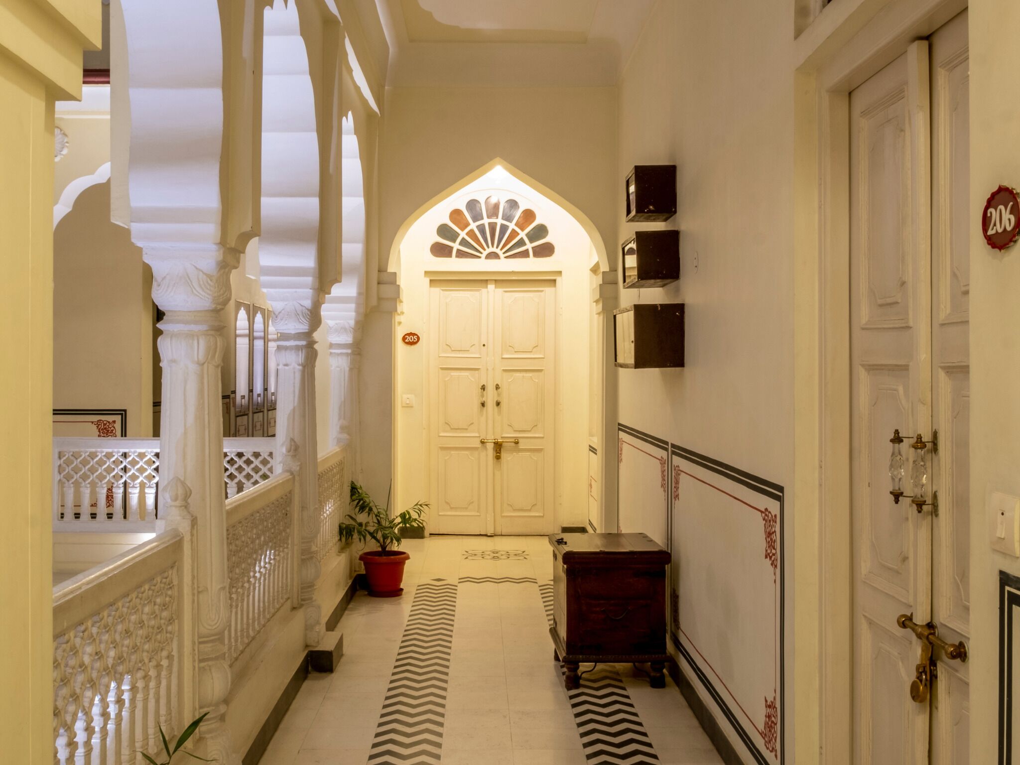 A corridor with a white door marked 206, a potted plant, and a small wooden chest.