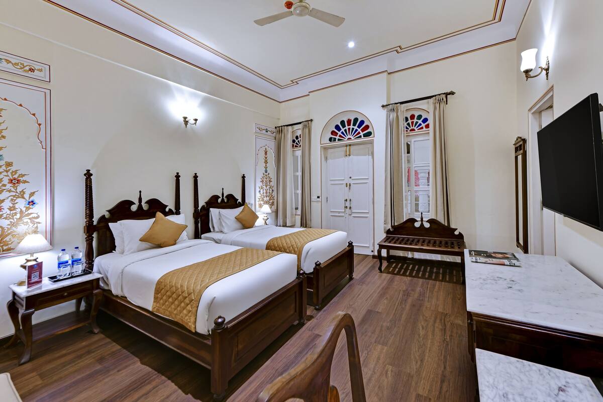 A hotel room with two wooden beds, a marble table, a ceiling fan, and a large mirror.