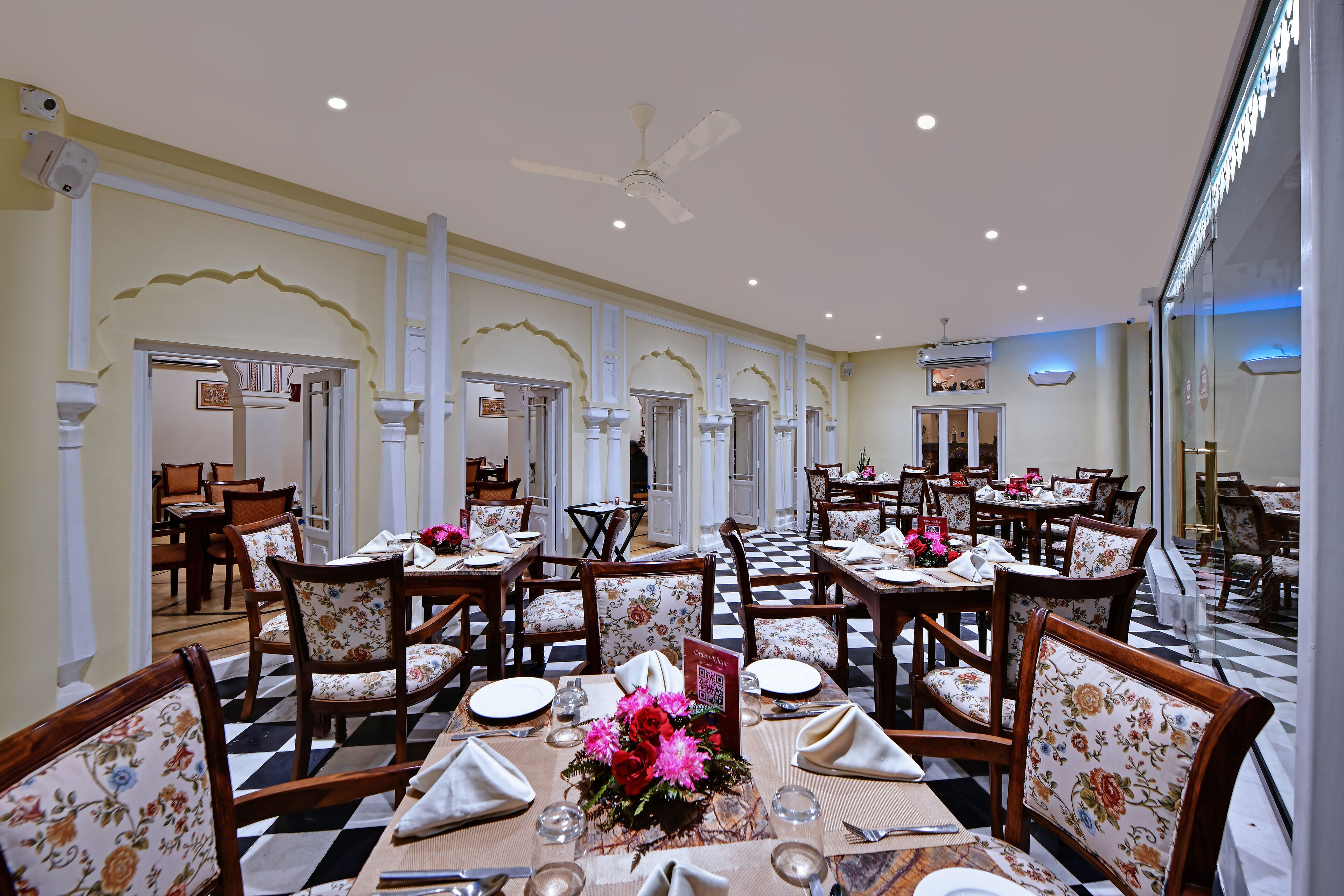 A dining area with checkered flooring, wooden tables, and floral upholstered chairs.