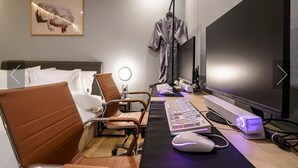 Una habitación de hotel moderna con cama, escritorio con ordenador, silla y un televisor de pantalla plana grande.