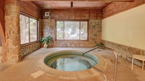 A stone-walled indoor swimming pool with a wooden ceiling, large windows, and a metal ladder. - Ocean Dunes 104 – Spacious oceanfront condo at Ocean Dunes in Kure Beach (Kure Beach)