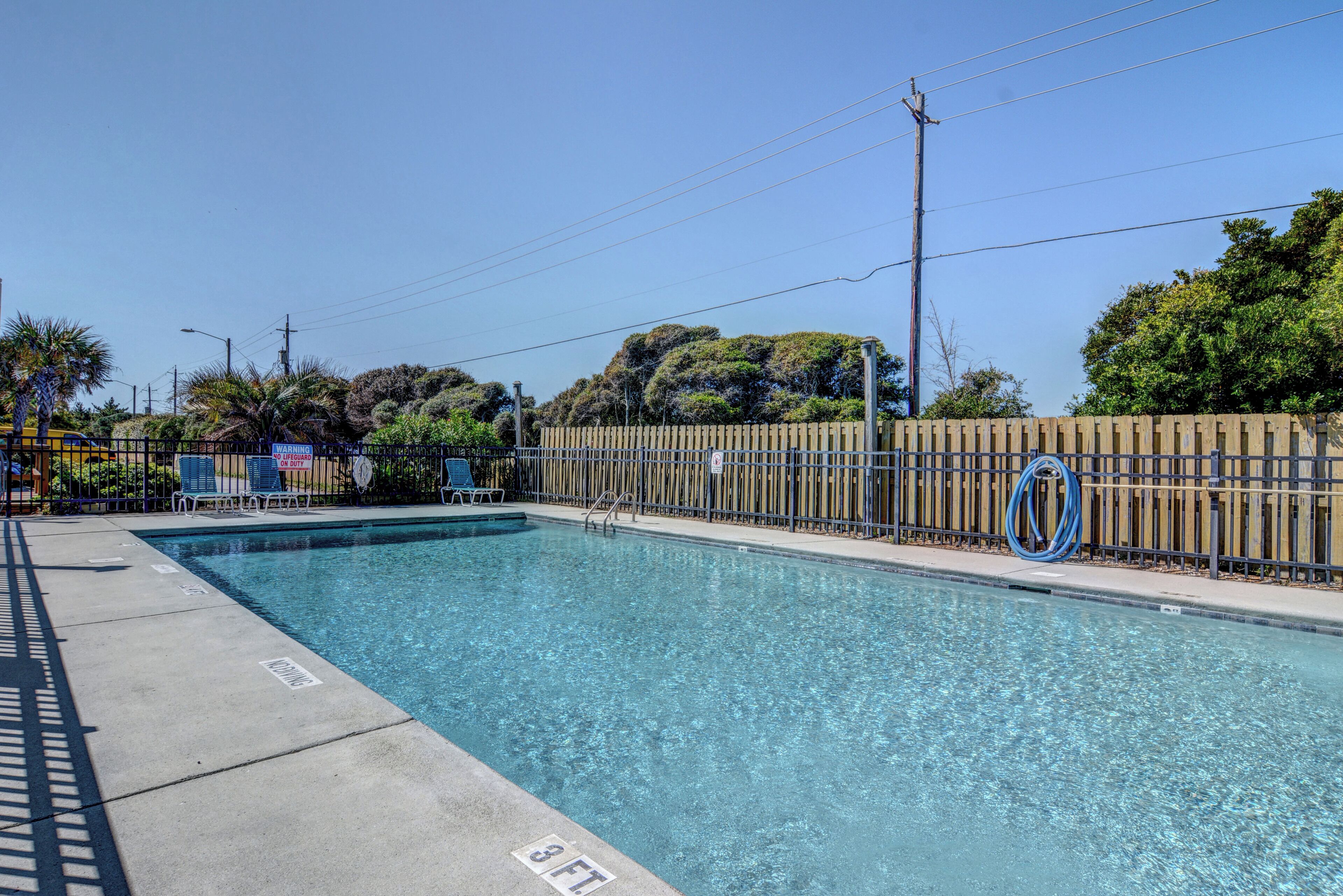 En rektangulär pool med klart, blått vatten, omgiven av ett trästaket och en betongplattform.