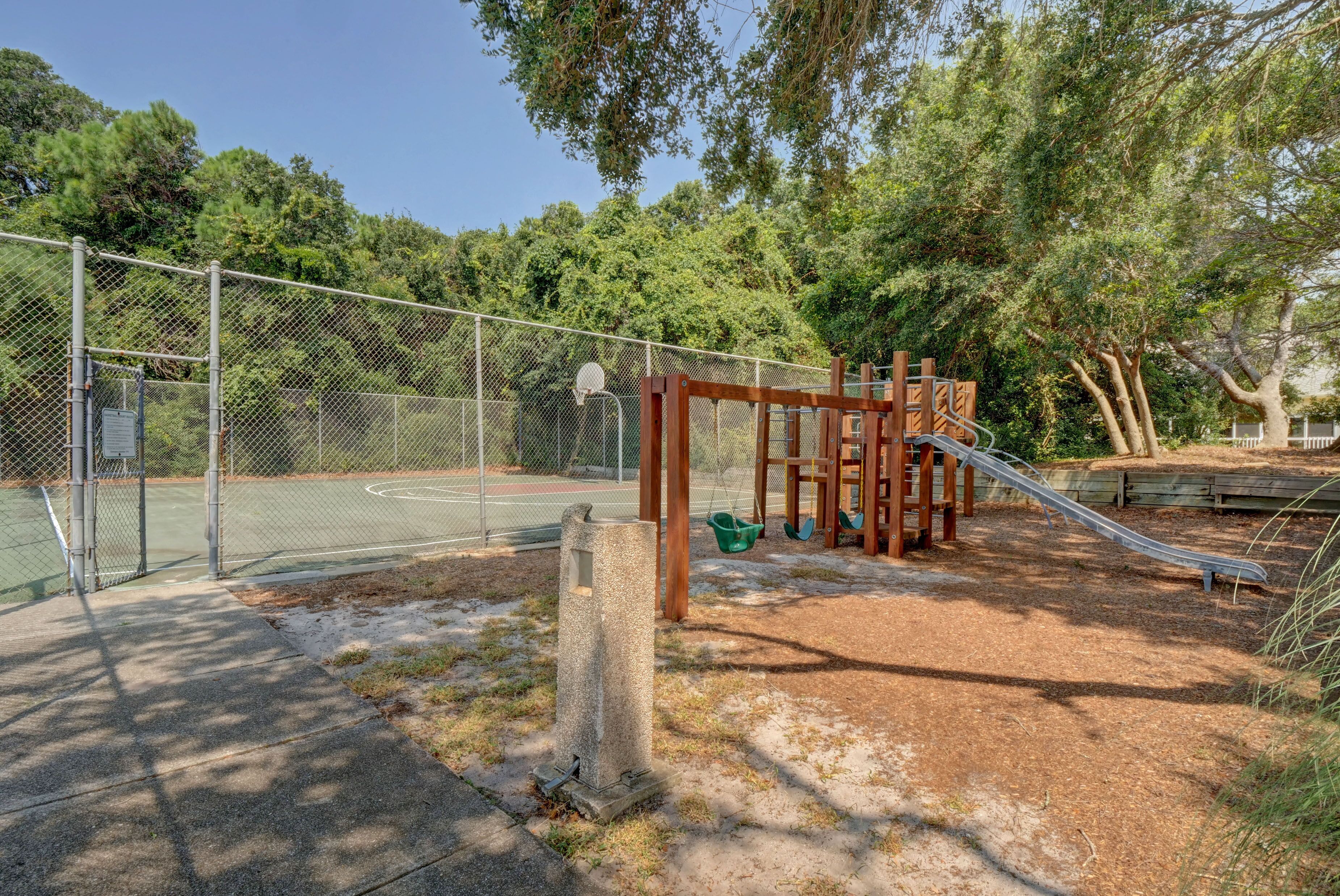 Un parque infantil con cancha de baloncesto, tobogán y columpios.