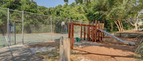 Un parque infantil con cancha de baloncesto, tobogán y columpios.