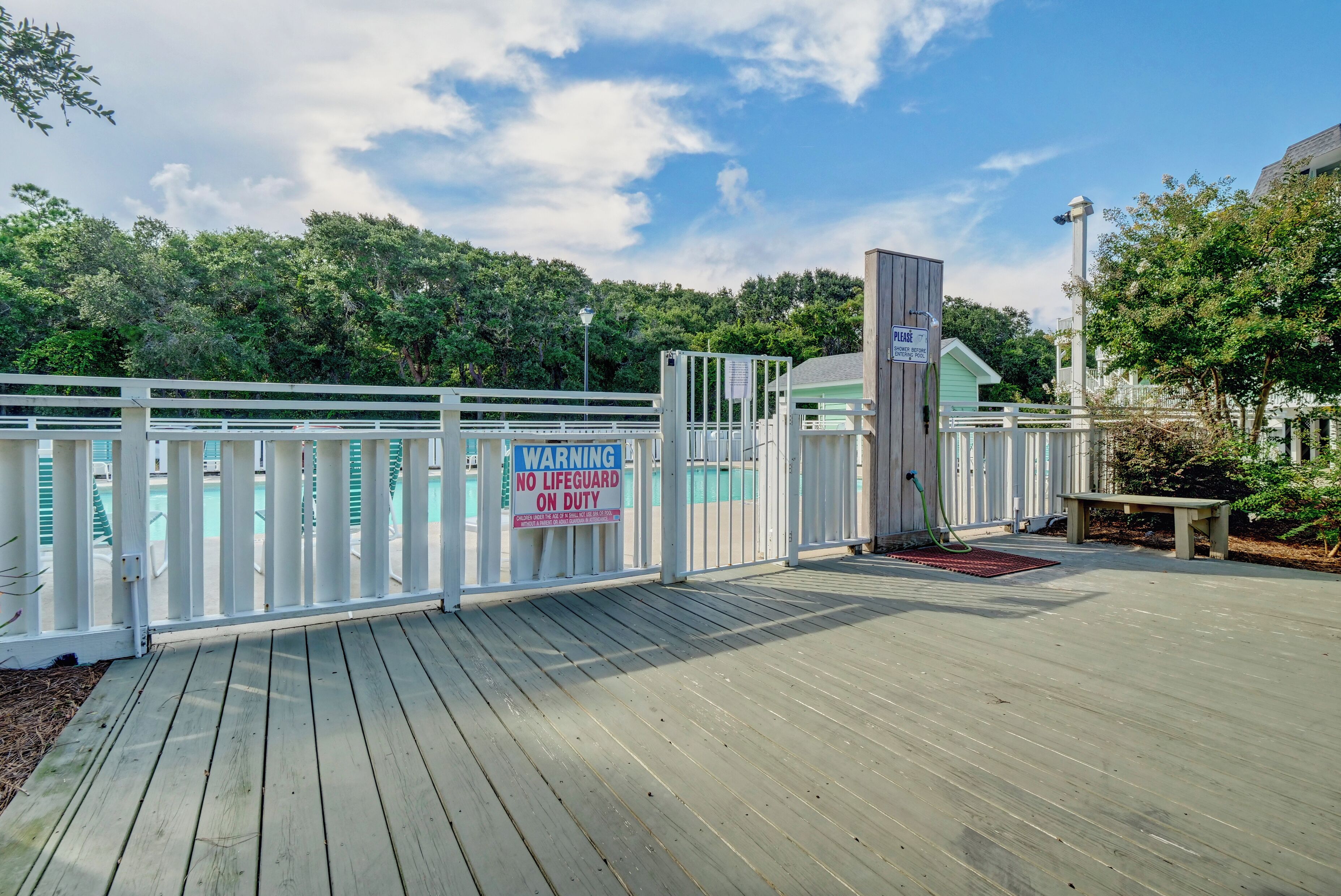 A wooden deck with a lifeguard warning sign, a pool, and a fenced area.