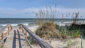 A wooden boardwalk leading to a beach with sand and grass. - Ocean Dunes 104 – Spacious oceanfront condo at Ocean Dunes in Kure Beach (Kure Beach)