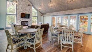 A spacious living room with a stone fireplace, large windows, and a pool view. - Ocean Dunes 104 – Spacious oceanfront condo at Ocean Dunes in Kure Beach (Kure Beach)
