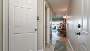 A hallway with white doors, a tiled floor, and a green rug leading to a room with a large window and a chair outside. - 1 Bedroom with Private Waterfront Balcony (Willis)