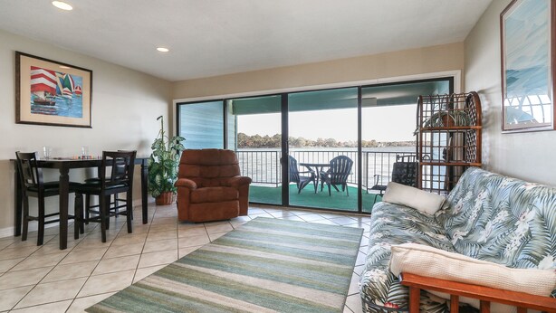 A living room with a dining area, a sofa, a chair, and a view of a balcony with chairs and a table. - 1 Bedroom with Private Waterfront Balcony (Willis)