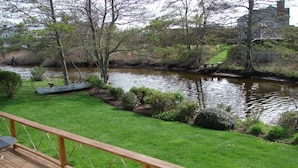 Eine Terrasse mit Geländer, die auf einen Fluss mit Grünpflanzen und einem kleinen Boot blickt.