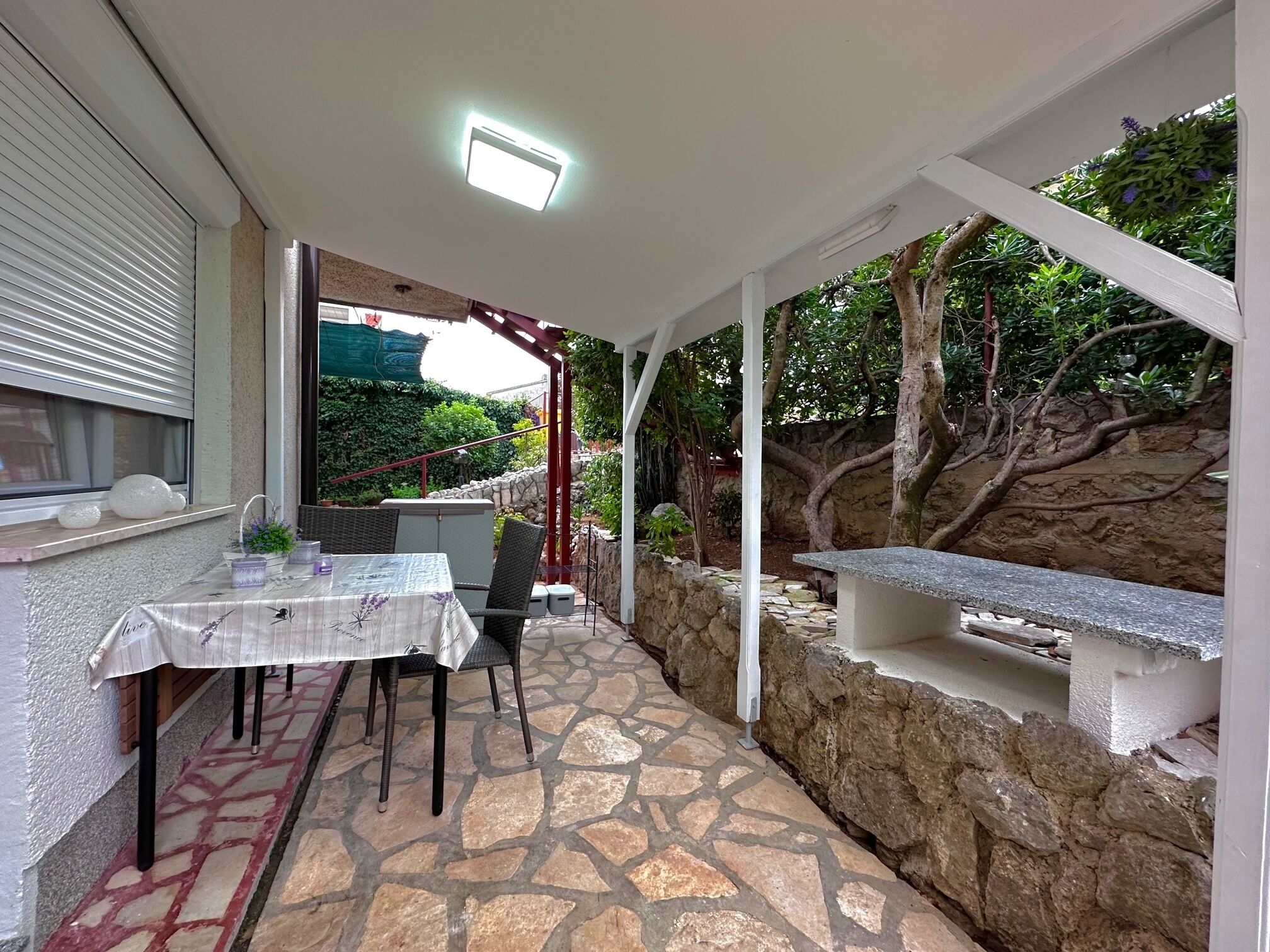 Un patio techado al aire libre con mesa y sillas, suelo de piedra y una pared de piedra.
