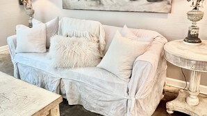 Un saló agradable amb un sofà de tons clars, una taula rodona petita i un quadre abstracte gran a la paret.