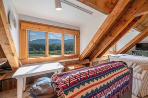 Une chambre confortable située dans les combles, avec une grande fenêtre donnant sur les montagnes, un plafond en bois et un lit confortable.