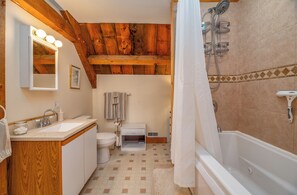 Une salle de bain avec un plafond en bois, une baignoire, une douche, un lavabo et des toilettes.