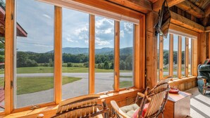 A wooden cabin with large windows offering a view of a road and greenery. There are two rocking chairs and a small table. - Mountain Lodge Retreat (Newry)