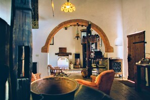 Cozy room with a fireplace, wooden table, and metal pot, set amidst exposed brickwork and wooden beams.