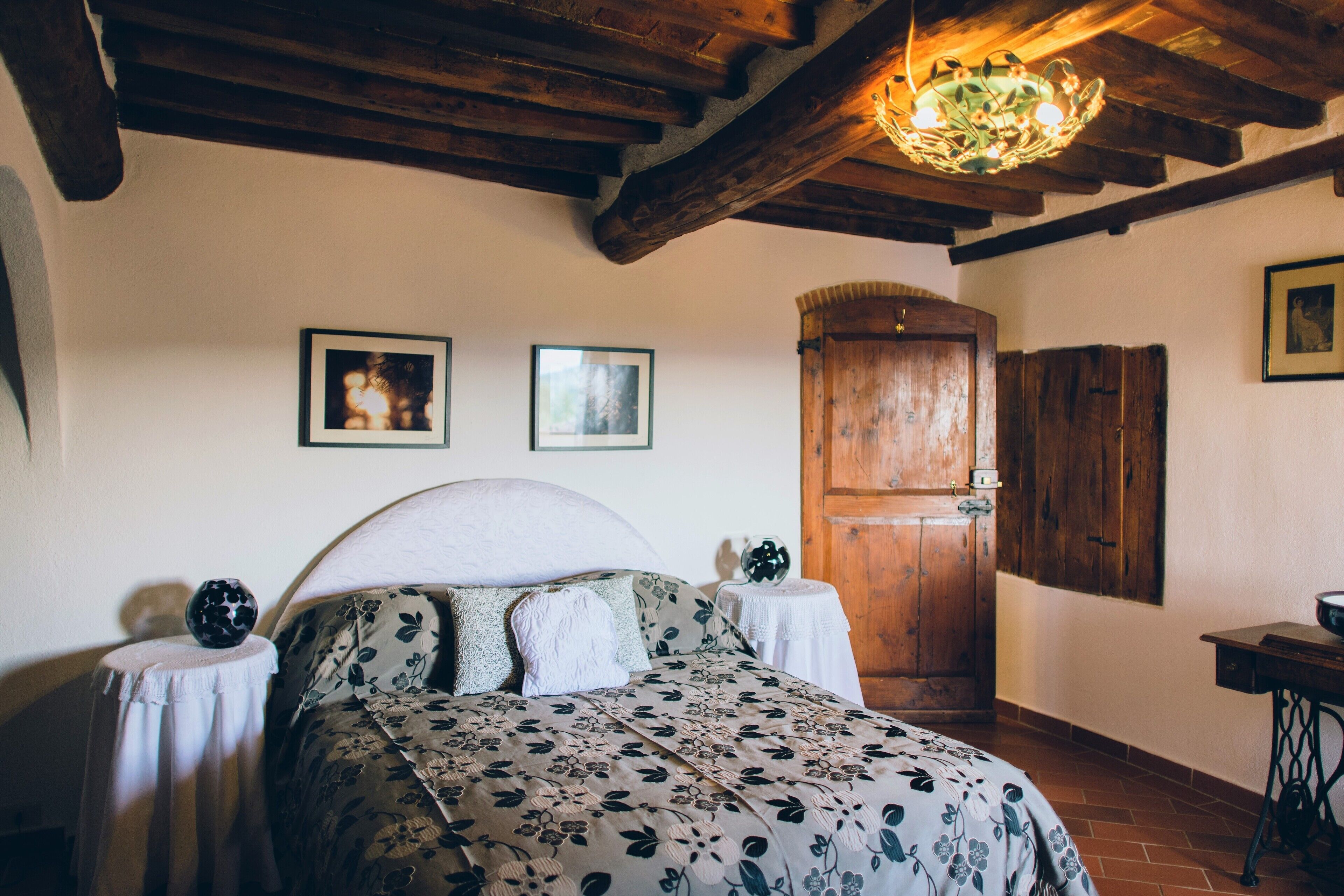 A bedroom with a bed, wooden ceiling beams, a wooden door, and framed pictures on the wall.