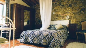 A bedroom with a stone wall, a canopy bed, a wooden chair, and a rustic wooden ceiling. - Beautiful historic 7-bedroom Villa on organic olive farm, pool & sunset views (Castellina in Chianti)