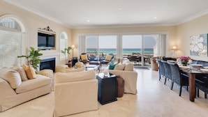 A spacious living room with a fireplace, comfortable seating, and a large window overlooking the ocean. - Tuscany Sunrise - A Luxury Retreat for Discerning Guests (Navarre)